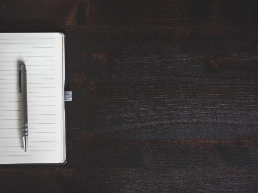 A notebook and pen on a dark wooden desk