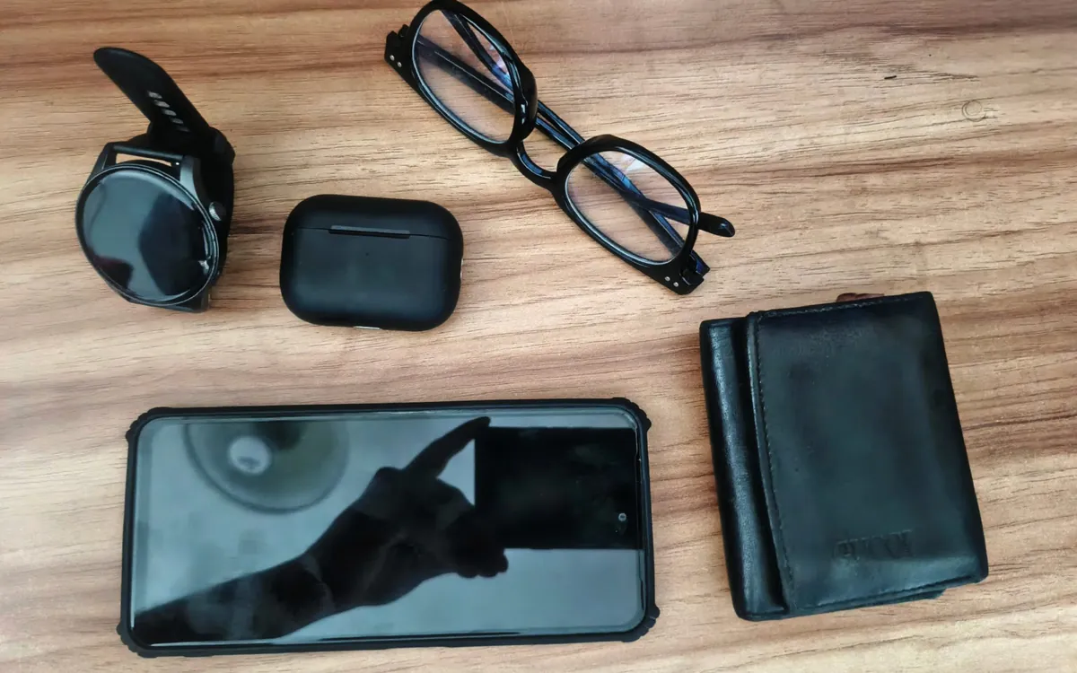 Phone, smartwatch, glasses and earbuds laid out on a wooden table