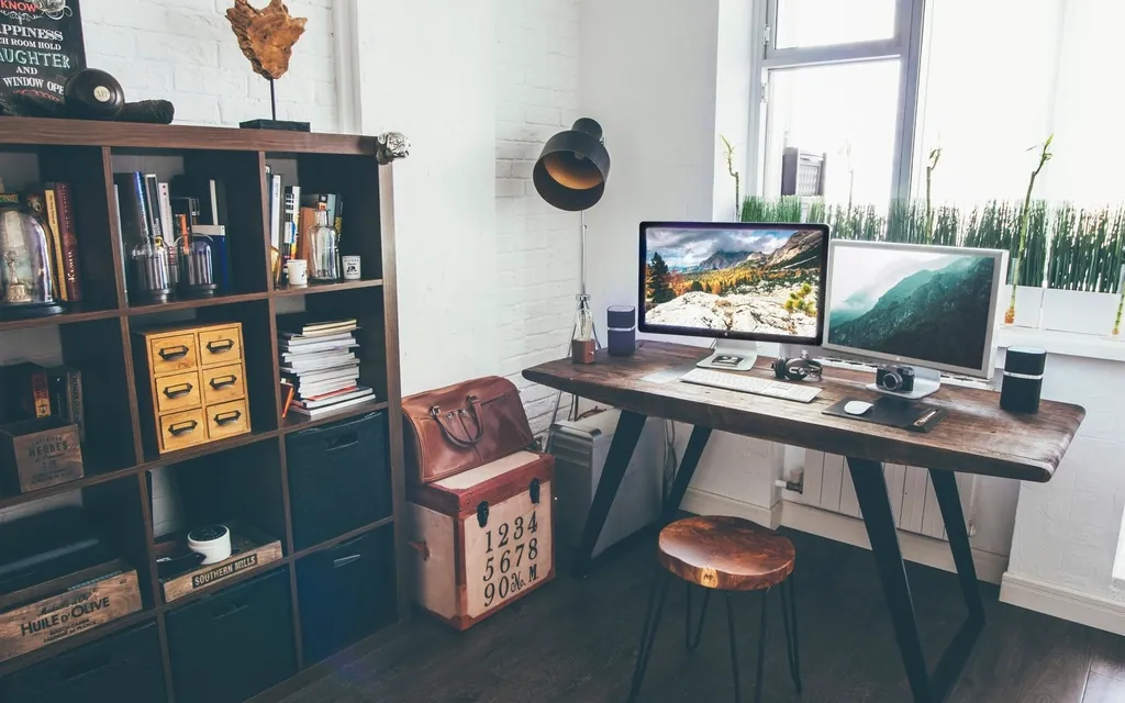 A home office desk with two monitors and a bookcase