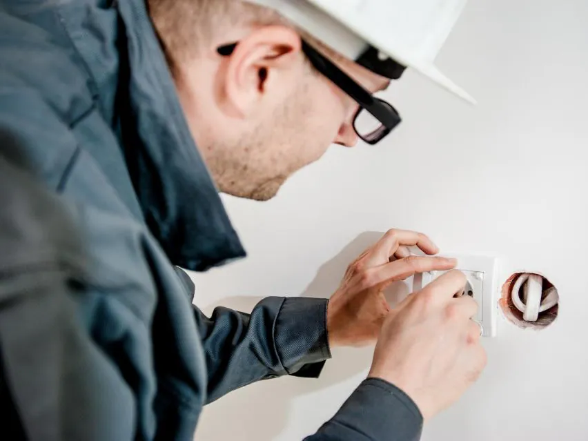 Electrician in a hard hat fitting a wall socket
