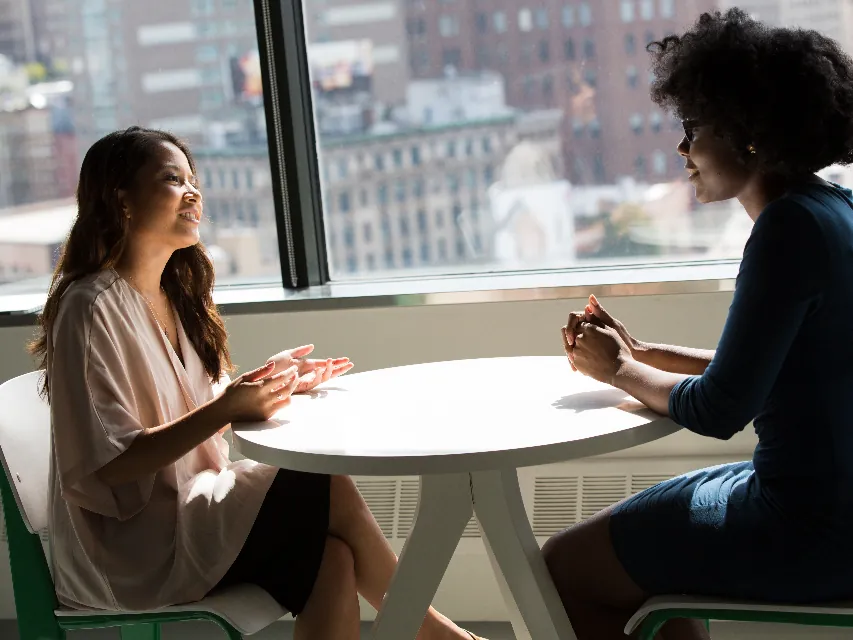 Two women in conversation at a table by a city window