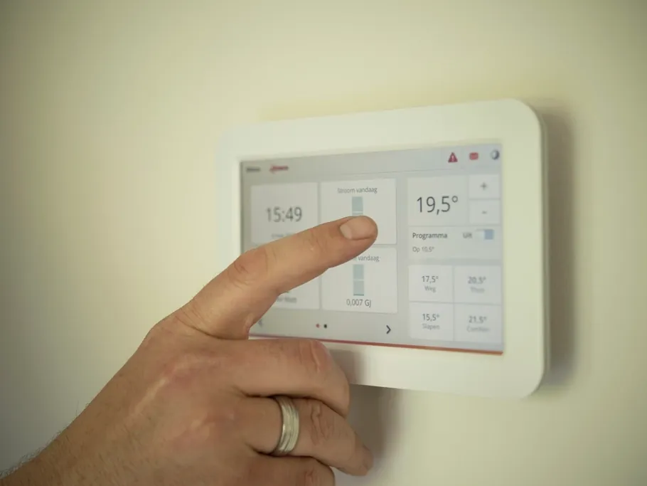 A hand adjusting a wall mounted smart thermostat