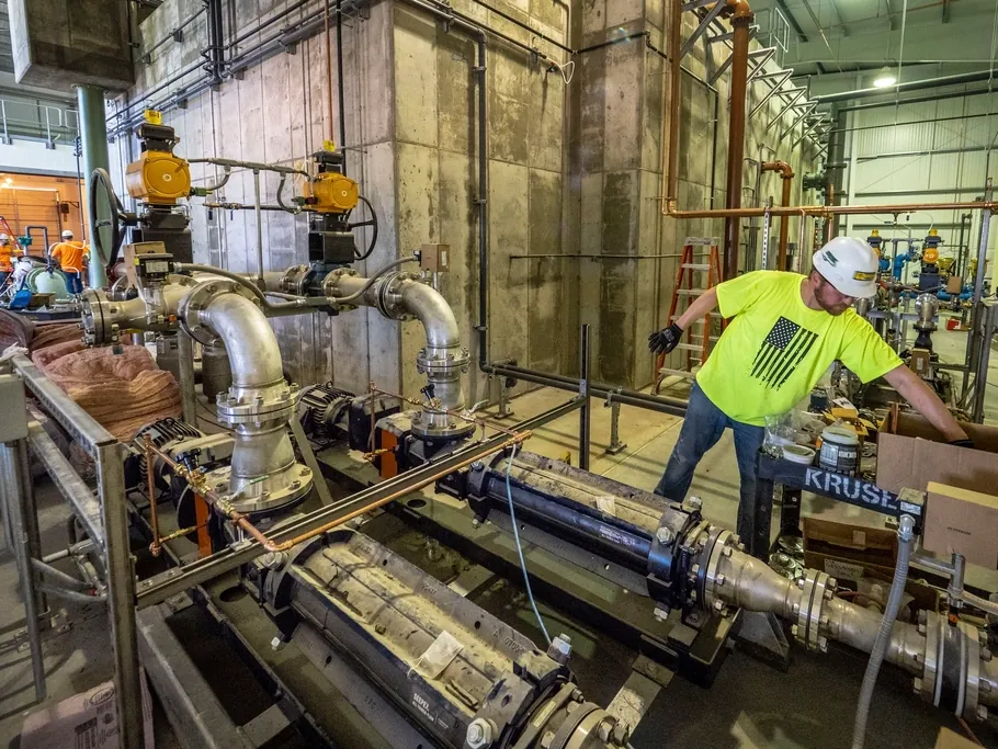 Pipefitter in a hi-vis vest working on pipework in a plant room