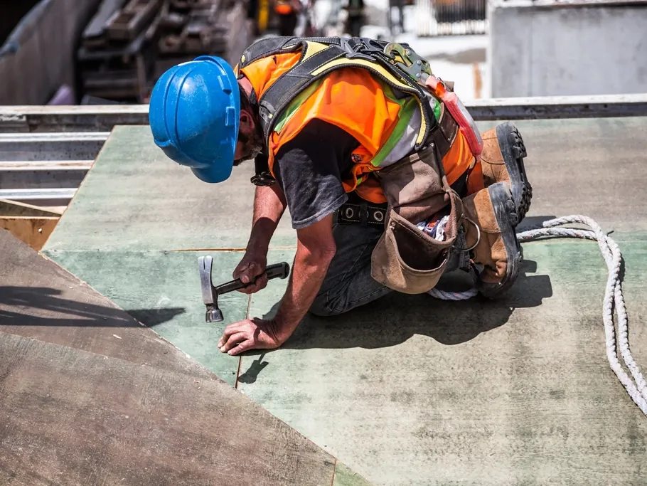 Roofer in safety gear nailing down a roof