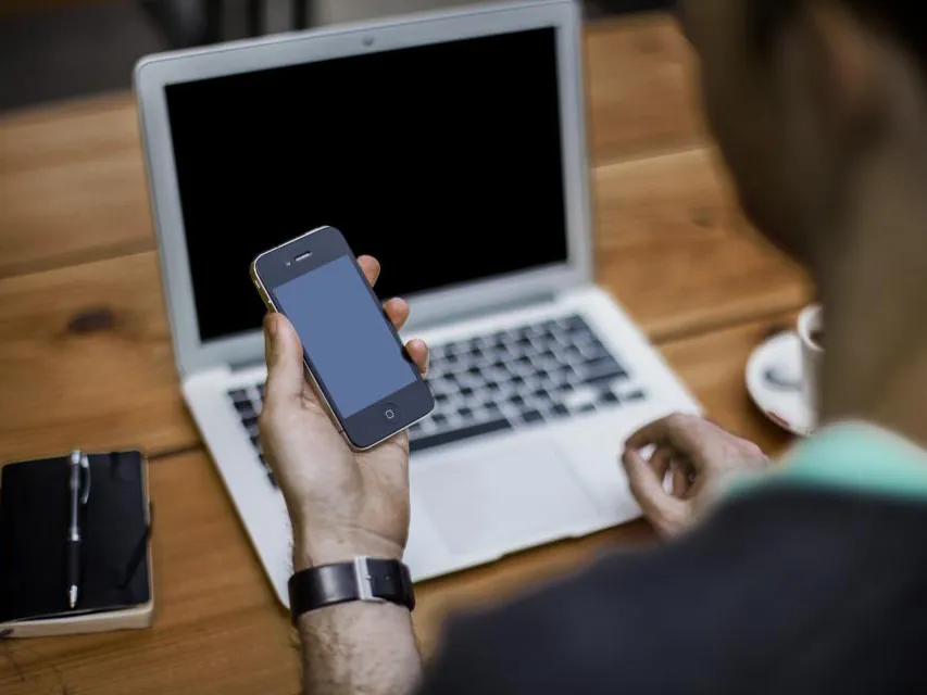 A phone held in front of an open laptop